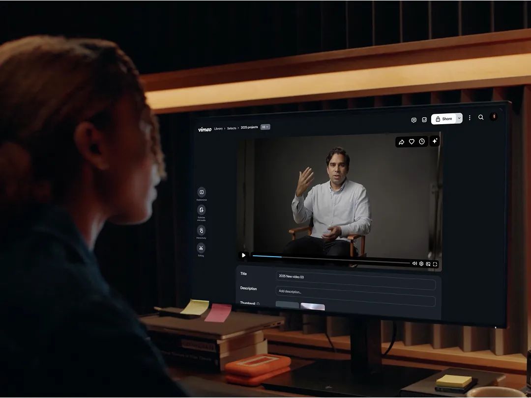 Person viewing a monitor displaying a video of a man in a collared shirt speaking and gesturing with his hands.